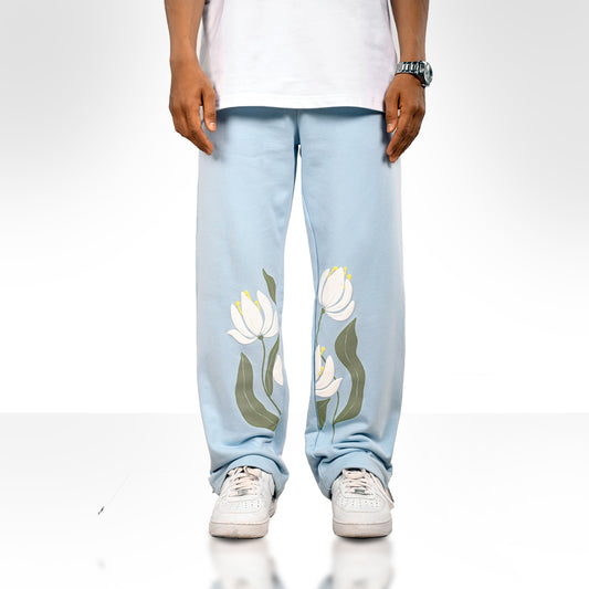 Light blue straight-leg pants with an elastic waistband and white lotus flower graphics with green leaves printed near the bottom of both legs, along with a small “forbidden” logo on the upper left side.