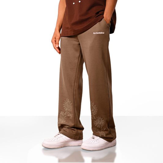 Brown straight-leg pants with a drawstring waist and beige sunflower embroidery near the bottom of both legs, along with a small “forbidden” text logo on the upper left side.