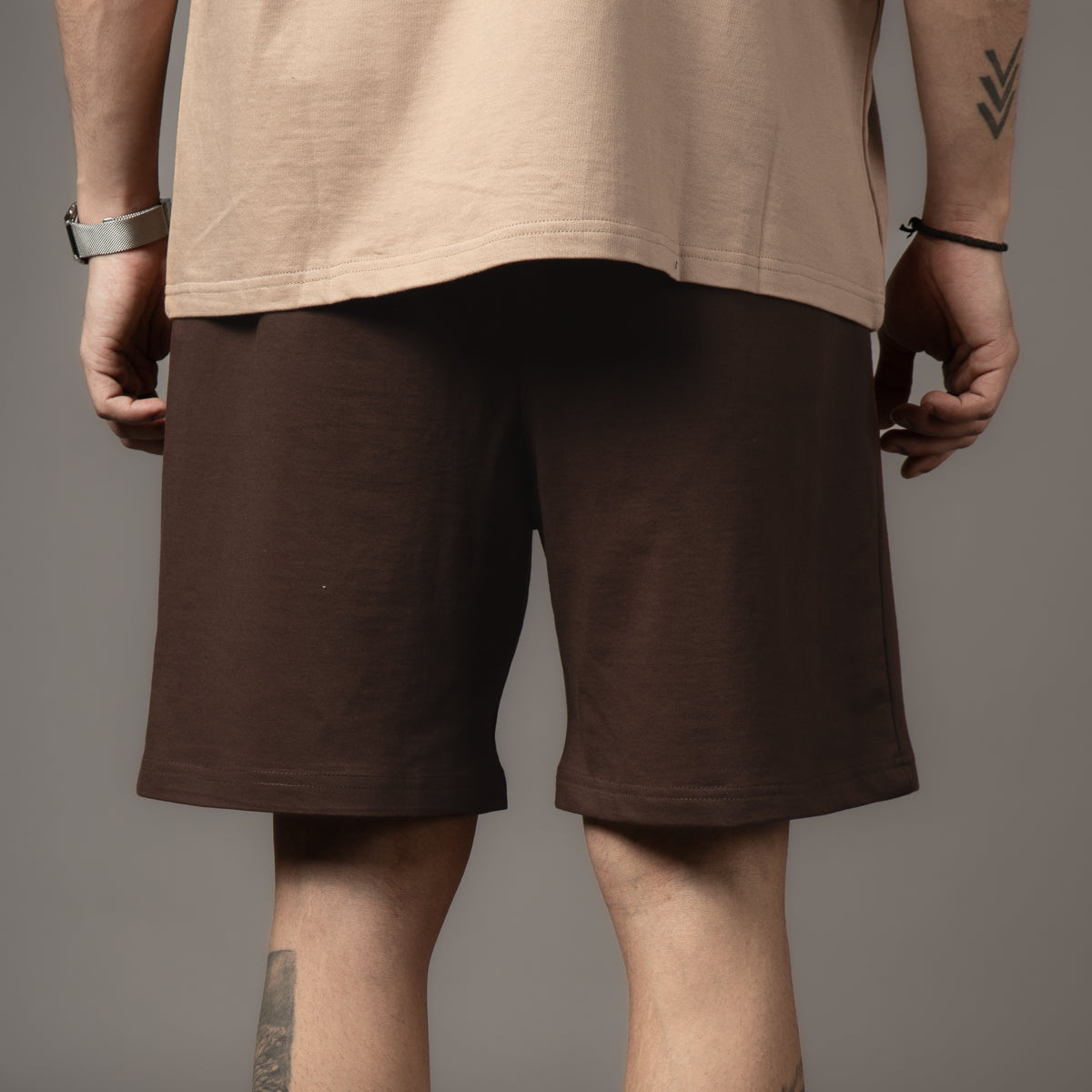 A person wearing brown shorts with a graphic of a sneaker and text "Who said ragers were not meant to fly." Casual vibe, neutral background.