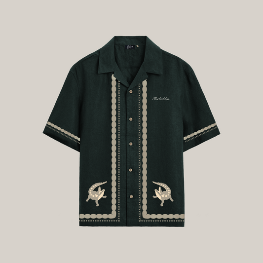 Dark green short-sleeve button-up shirt with cream embroidered borders, decorative stitch detailing, crocodile motifs near the hem, and “Forbidden” text on the chest.