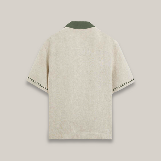 Short-sleeve beige button-up shirt with a dark green collar, featuring decorative stitching on the sleeves and two stylized brown cheetah graphics with green leaves near the hem, along with the word “Forbidden” embroidered on the chest.