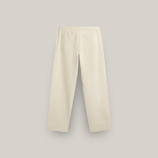 Cream-colored straight-leg pants with an elastic waistband and pink “forbidden” text on the upper left side, featuring floral prints with pink blossoms, green leaves, and black dots near the bottom of both legs.