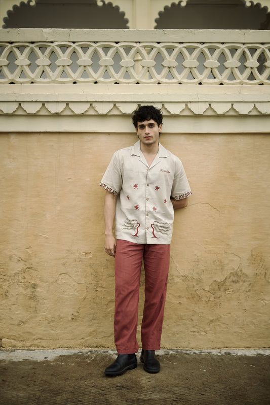 Short-sleeve beige button-up shirt, featuring decorative on the sleeves and two stylized tree graphics with star along with the word “Forbidden” embroidered on the chest.