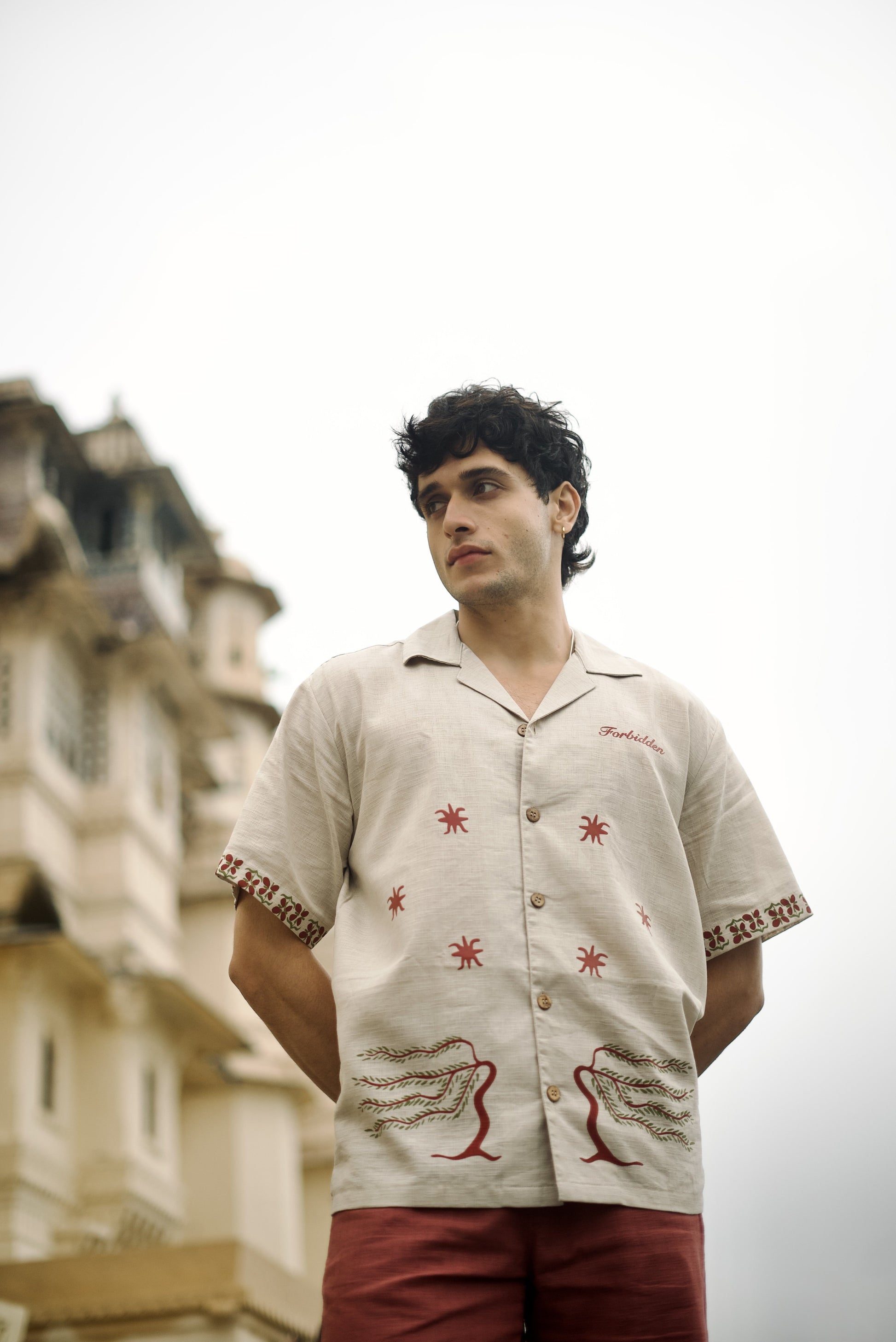 Short-sleeve beige button-up shirt, featuring decorative on the sleeves and two stylized tree graphics with star along with the word “Forbidden” embroidered on the chest.