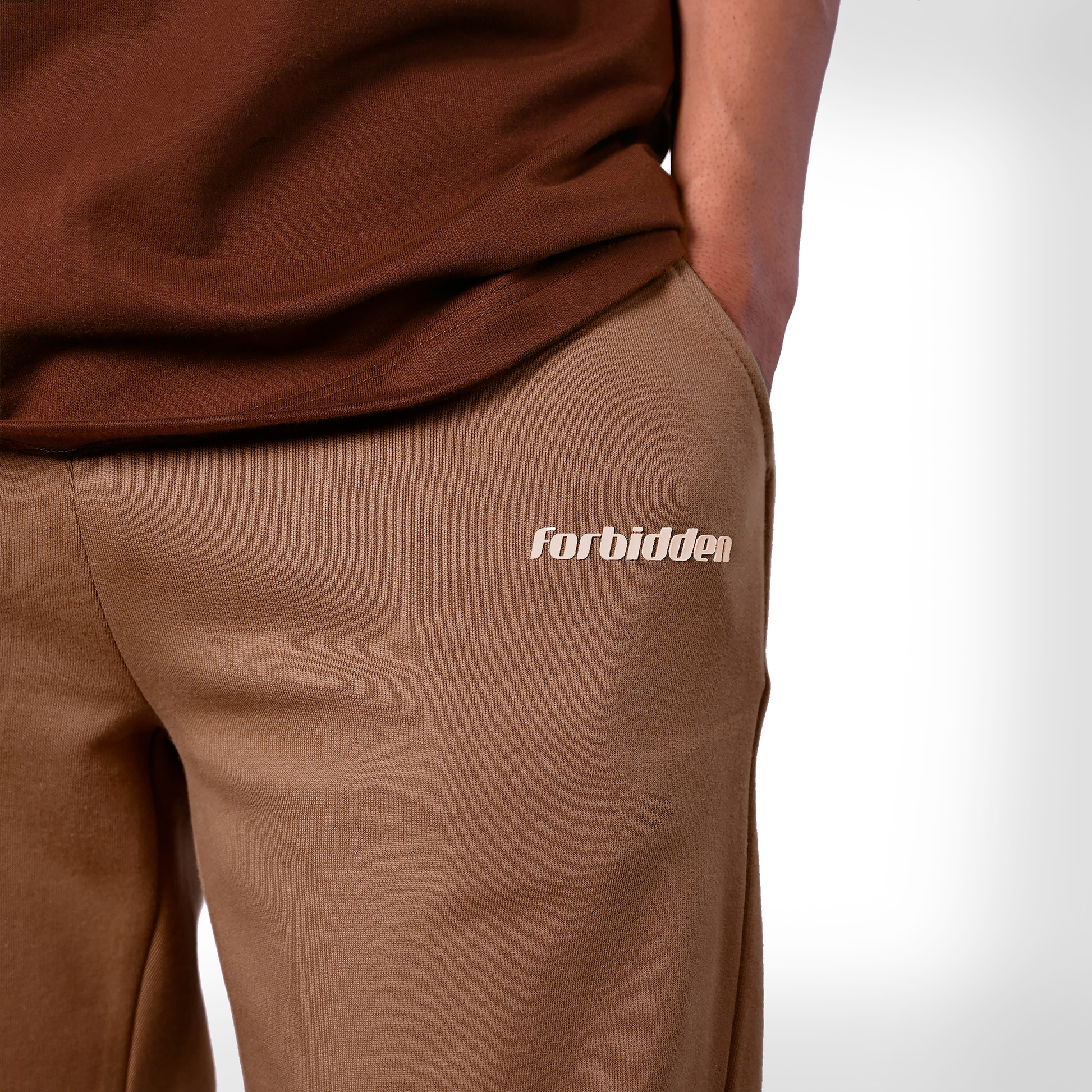 Brown straight-leg pants with a drawstring waist and beige sunflower embroidery near the bottom of both legs, along with a small “forbidden” text logo on the upper left side.