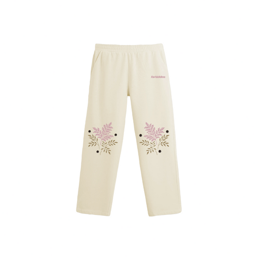 Cream-colored straight-leg pants with an elastic waistband and pink “forbidden” text on the upper left side, featuring floral prints with pink blossoms, green leaves, and black dots near the bottom of both legs.