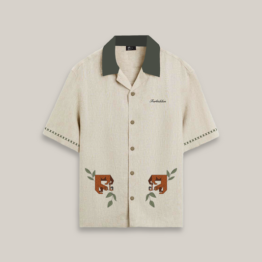 Short-sleeve beige button-up shirt with a dark green collar, featuring decorative stitching on the sleeves and two stylized brown cheetah graphics with green leaves near the hem, along with the word “Forbidden” embroidered on the chest.