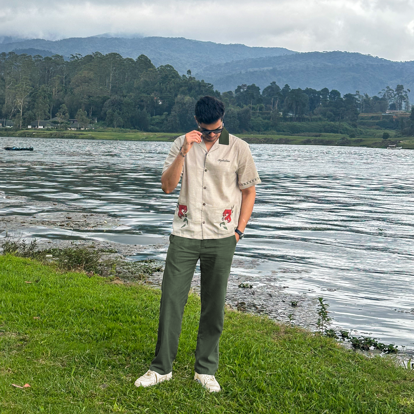 Short-sleeve beige button-up shirt with a dark green collar, featuring decorative stitching on the sleeves and two stylized brown cheetah graphics with green leaves near the hem, along with the word “Forbidden” embroidered on the chest.