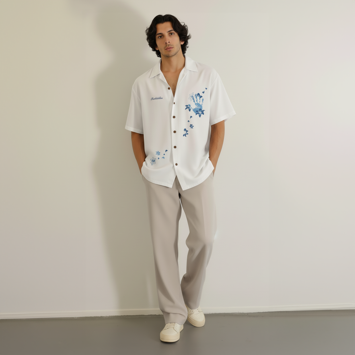 The design includes layered flowers, petals, and small decorative elements in varying shades of blue. The word "Forbidden" is embroidered on the left chest in a small script font. The buttons are metallic or bronze-toned, adding a subtle contrast to the clean white shirt. The overall aesthetic is elegant, artistic, and slightly whimsical.